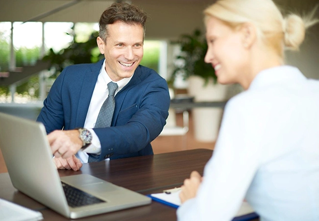 A man and woman sitting at a table with a laptop.