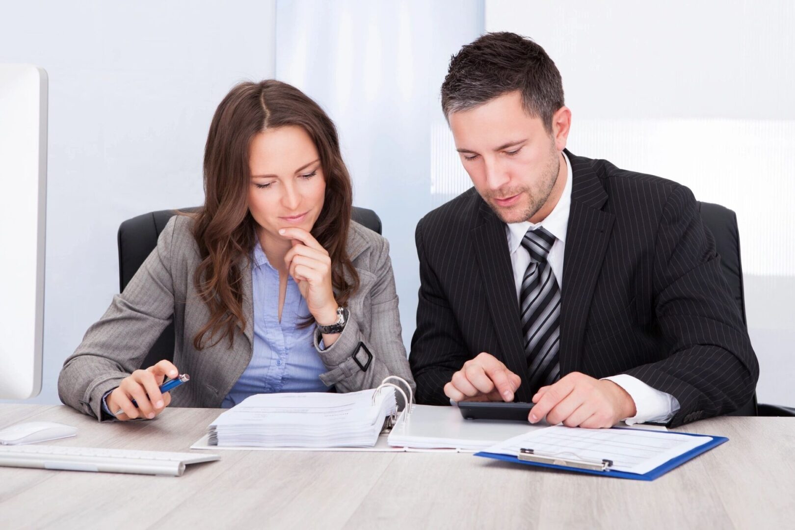 Two people sitting at a table with papers and calculators.